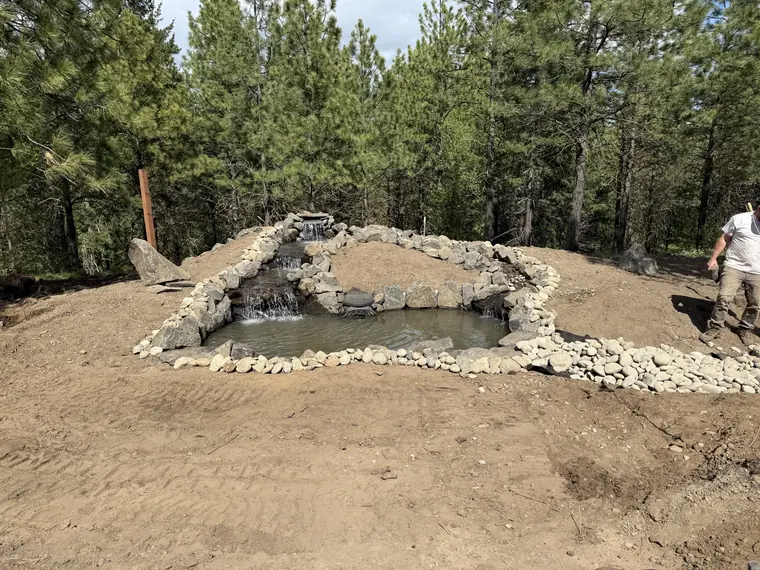 Pond basin shaped and edged with stone, surrounded by bare graded soil