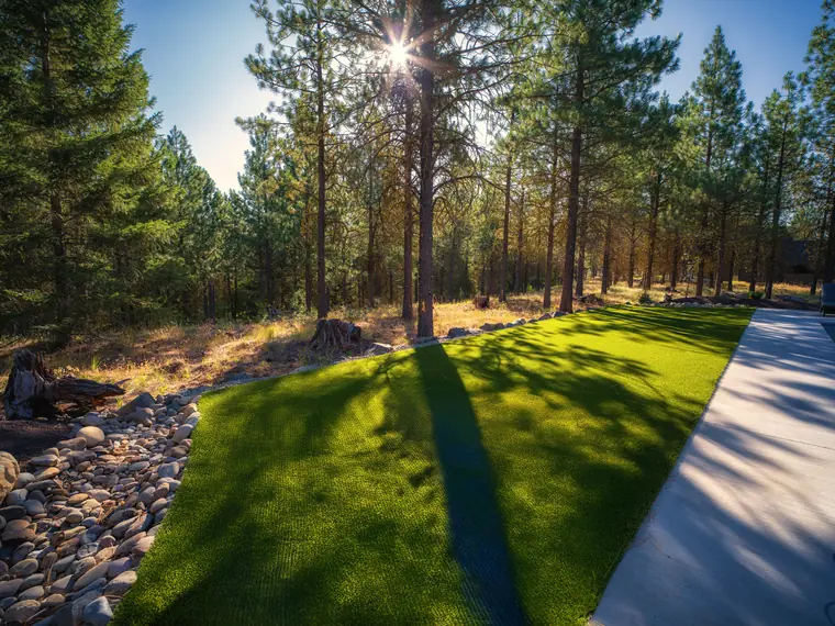 Artificial turf lawn edged with river rock beside a concrete walk